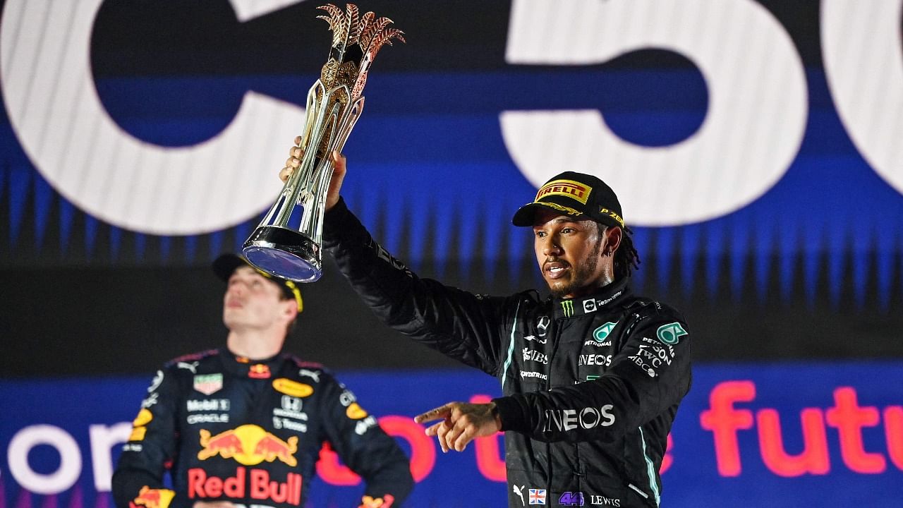 Winner Mercedes' British driver Lewis Hamilton (R) reacts with his trophy flanked by second-placed Red Bull's Dutch driver Max Verstappen (L) during the podium ceremony after the Formula One Saudi Arabian Grand Prix at the Jeddah Corniche Circuit in Jeddah on December 5, 2021. Credit: AFP Photo
