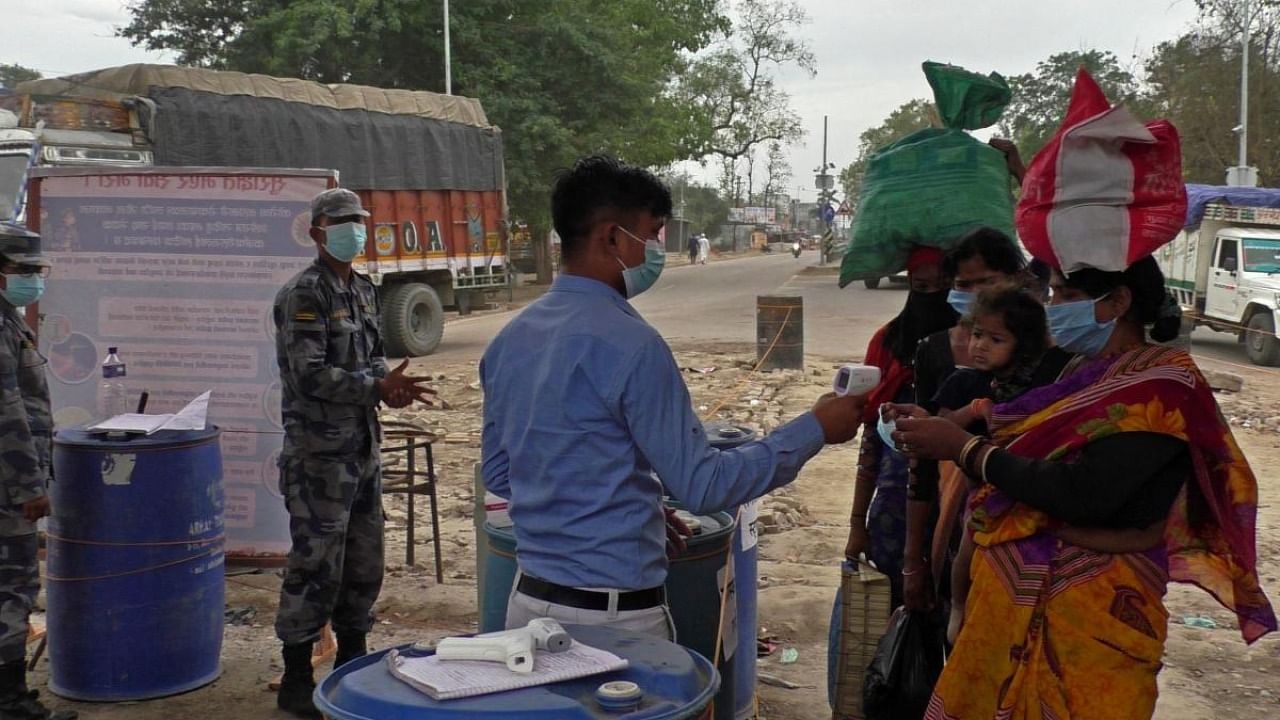 An official checks the body temperature of Nepali migrant workers as a preventive measure against the Covid-19 coronavirus, as they walk across the India-Nepal border to return back to Nepal, in Jamunaha near Nepalgunj. Credit: AFP file photo