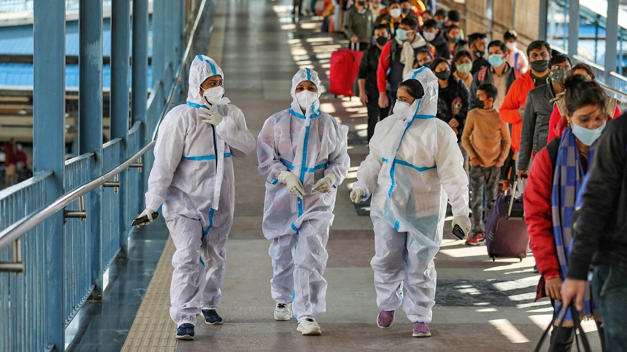 Health workers walk past the passengers waiting in a queue during Covid-19 testing at Katra railway station, amid the threat of spreading of the new Covid-19 variant 'Omicron'. Credit: PTI File Photo