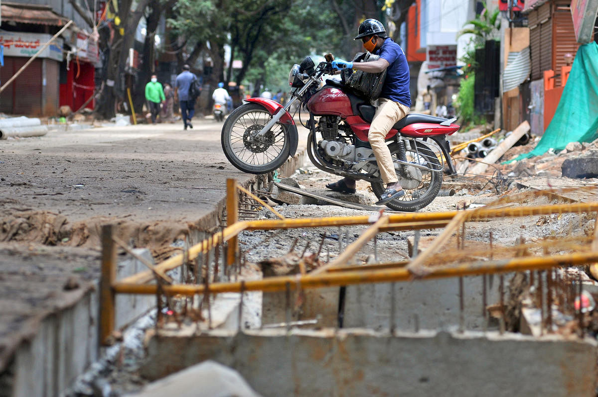 People with two-wheeler try to cross at the on-gong TenderSURE work at Gandhinagar in Bengaluru. Credit: DH Photo