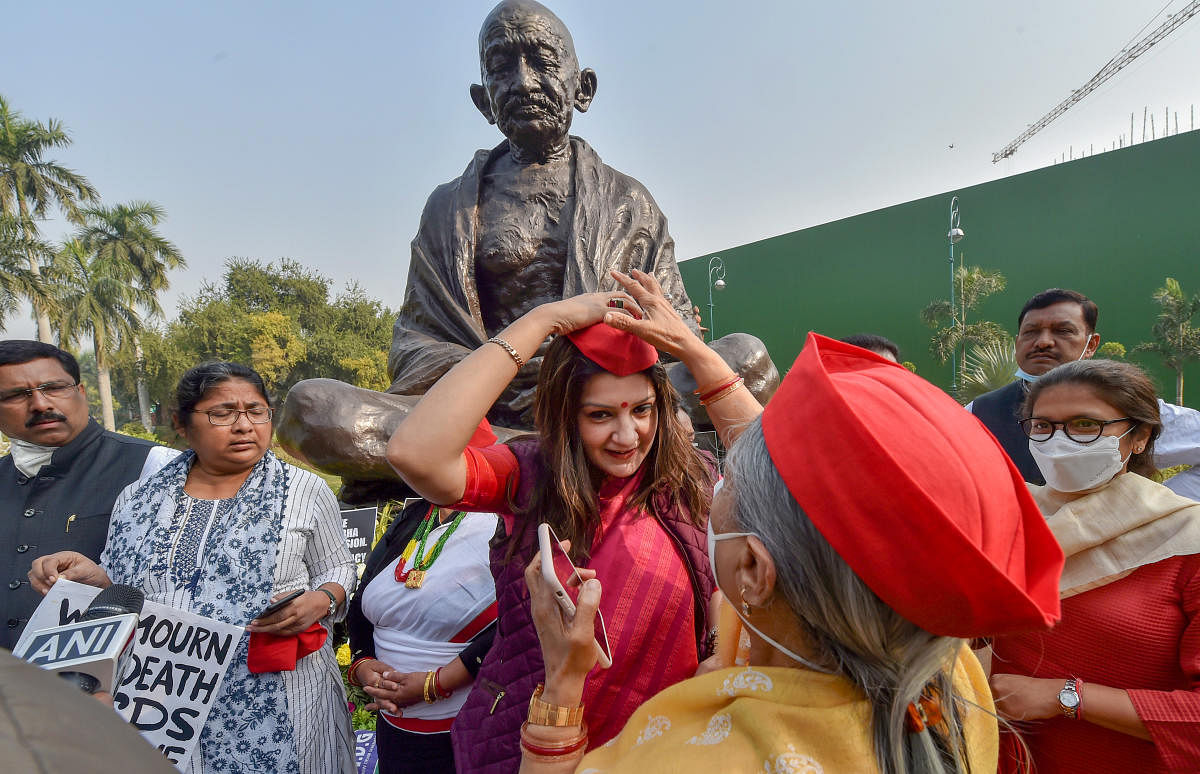 Shiv Sena MP Priyanka Chaturvedi wears the red cap given by SP MP Jaya Bachchan, during a protest of suspended Rajya Sabha MPs demanding revocation of their suspension, amid the ongoing Winter Session of Parliament. Credit: PTI Photo