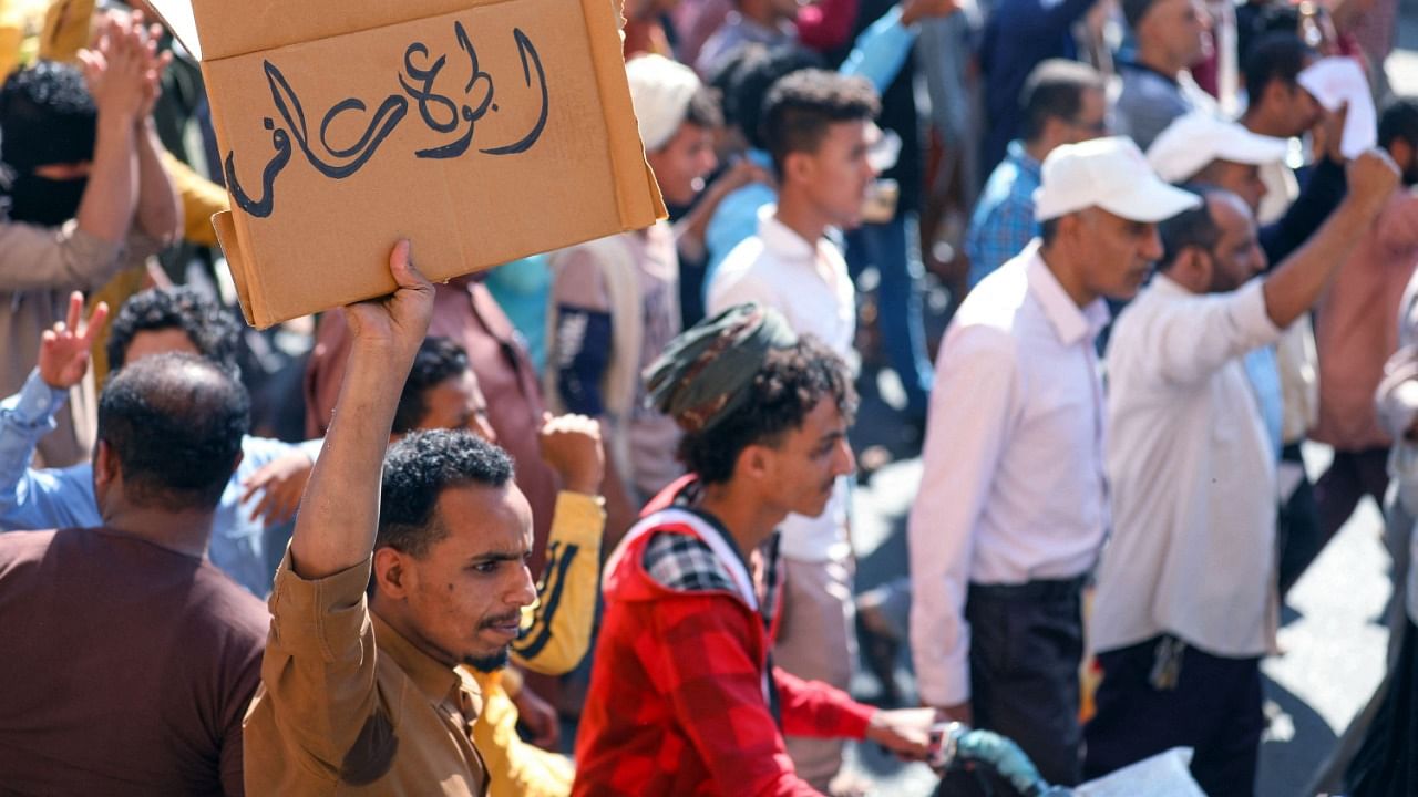 Yemenis chant slogans during protests calling for the removal of the Saudi-backed coalition government and denouncing economic and living conditions, in Yemen's third city of Taez, on December 5, 2021. The placard in Arabic reads "Hunger is Godless". Credit: AFP File Photo