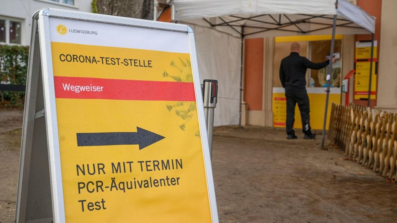 A sign shows the way to a PCR Covid-19 test station as a man stands at its window in Hemmingen near Ludwigsburg, southern Germany, on December 7, 2021, amidst the ongoing coronavirus pandemic. Credit: AFP Photo