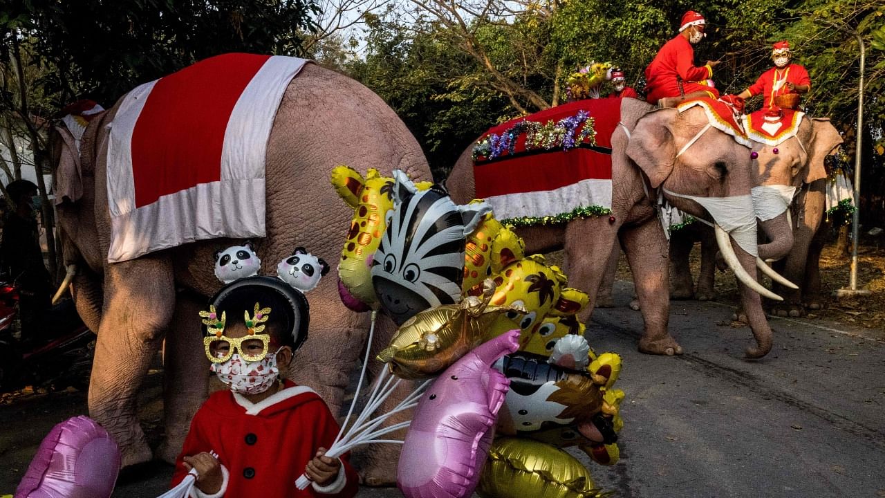 A child wearing a festive outfit holds balloons as mahouts and their elephants prepare to take part in Christmas celebrations at the Jirasart Witthaya school in Ayutthaya. Credit: AFP Photo