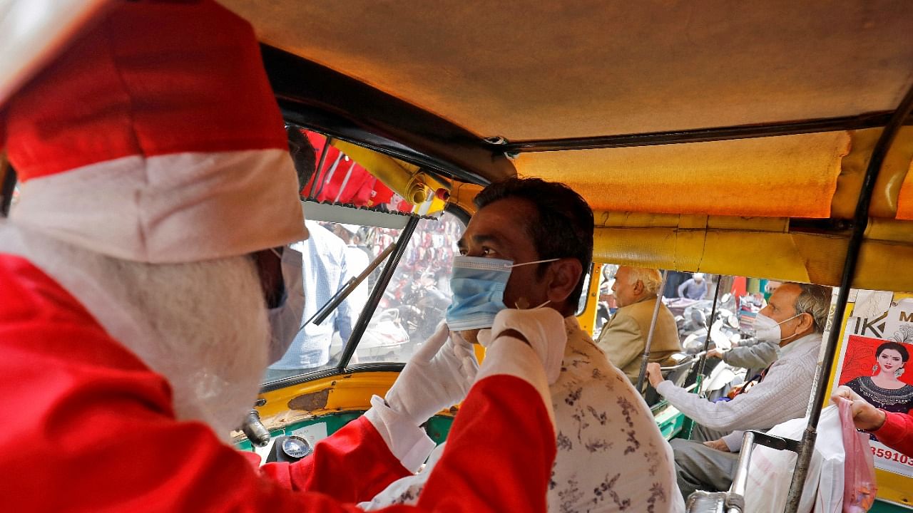 A man wearing a Santa Claus costume helps an auto-rickshaw driver to wear a protective face mask, in Ahmedabad. Credit: Reuters Photo