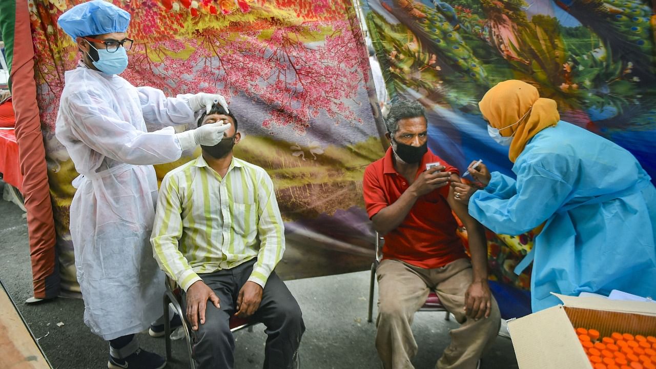 A health worker conducts Covid-19 testing of a person while another administers a dose of COVID vaccine , during a 'vaccination mela' outside a bus terminal at Parimpora in Srinagar. Credit: PTI File Photo