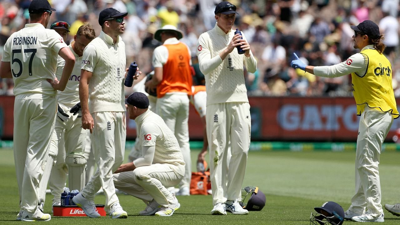 England's Rory Burns (R) provides drinks to players while wearing rubber gloves on day two of the third Ashes cricket Test match between Australia and England in Melbourne on December 27, 2021. Credit: AFP Photo