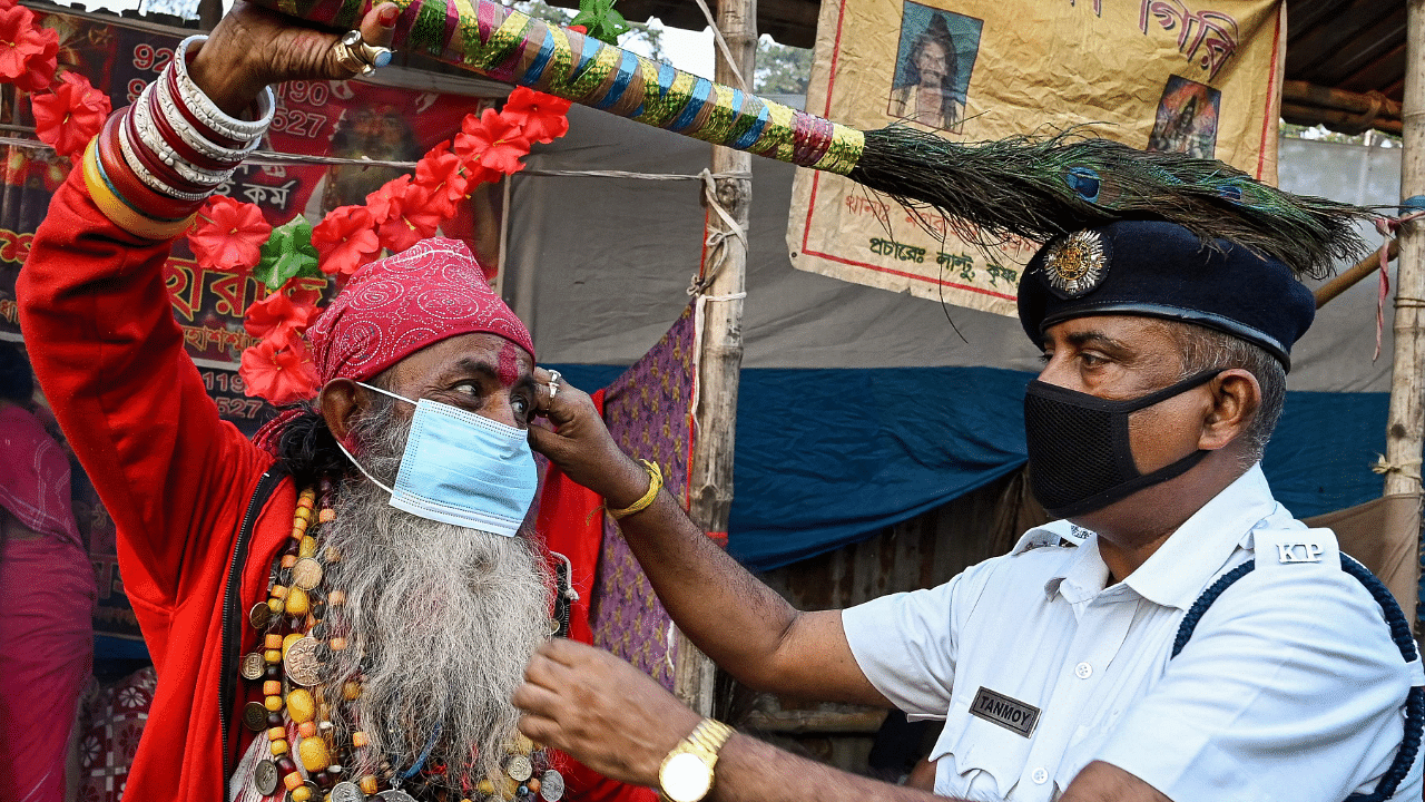 A police personnel distributes face masks to pilgrims encouraging them to follow Covid-19 coronavirus safety protocols at a transit camp ahead of the upcoming annual religious Gangasagar Mela. Credit: AFP Photo