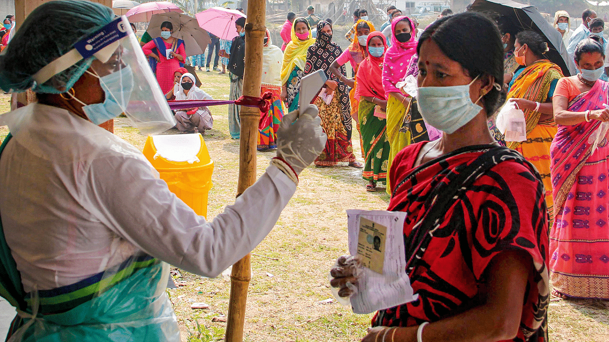 A health worker sanitises voters as they wait in queues to cast votes at a polling station. Credit: PTI Photo