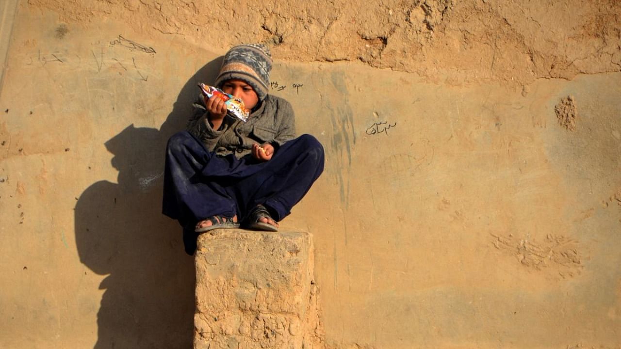 An Afghan boy snacks while sitting on a plinth besides a mud house in Kandahar city on January 8, 2022. Credit: AFP Photo