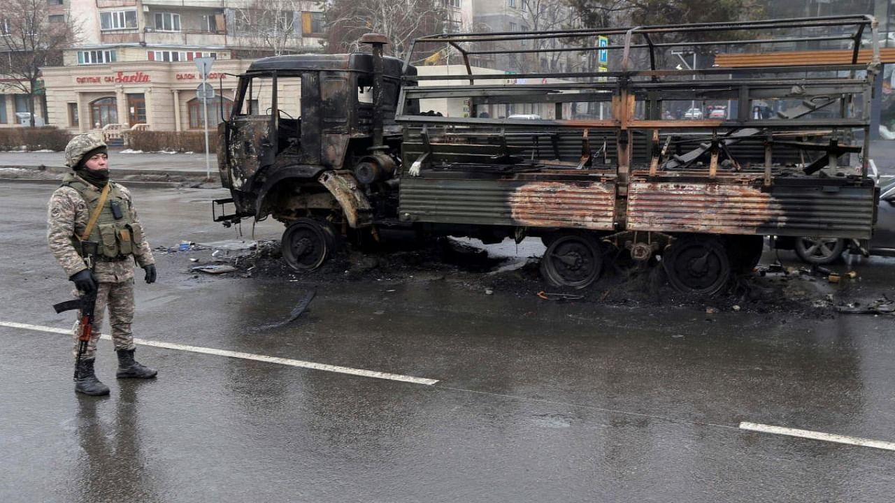 A Kazakh law enforcement officer stands guard near a burnt truck while checking vehicles in a street following mass protests triggered by fuel price increase in Almaty, Kazakhstan. Credit: Reuters Photo