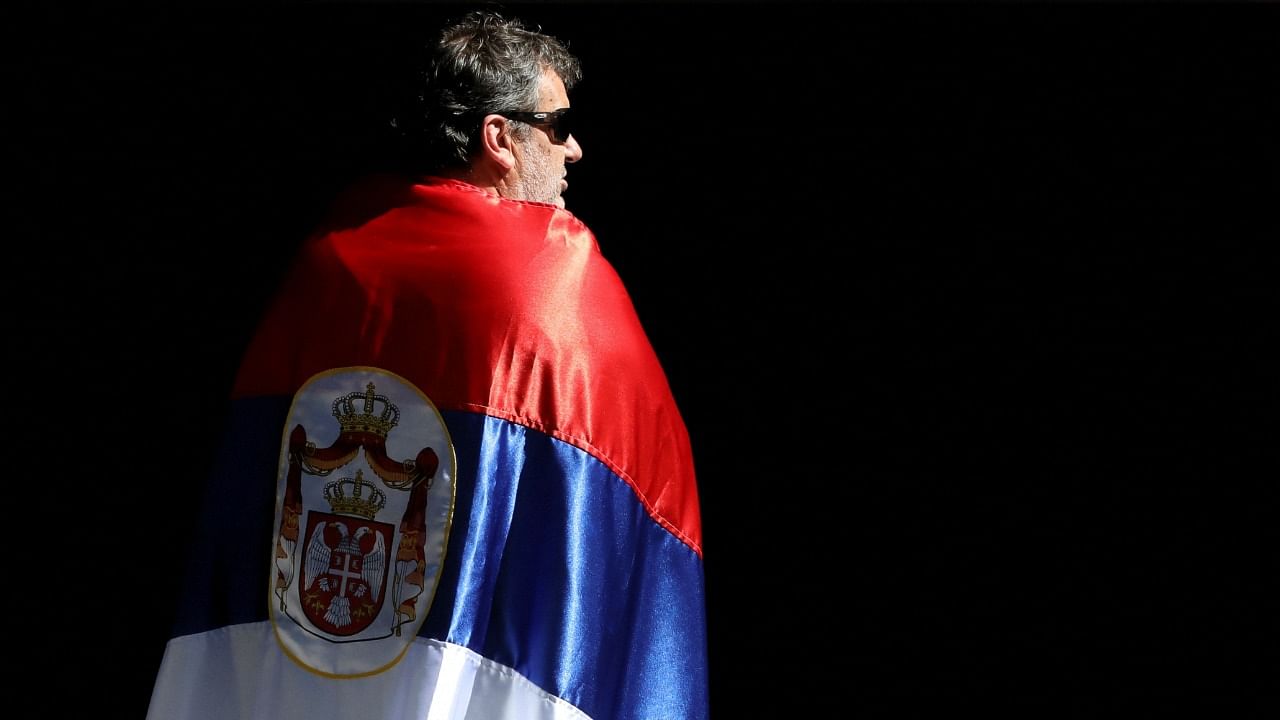 A supporter of Serbian tennis player Novak Djokovic waits draped in a Serbian flag, as Djokovic attends a court hearing at the offices of his legal team, after his visa to play in the Australian Open was cancelled a second time and he was placed back in immigration detention, in Melbourne, Australia, January 16, 2022. Credit: Reuters Photo