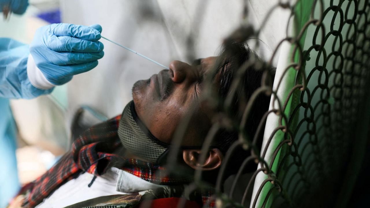 A healthcare worker collects a Covid-19 test swab sample from a man, amidst the spread of the disease, at a railway station in New Delhi. Credit: Reuters photo