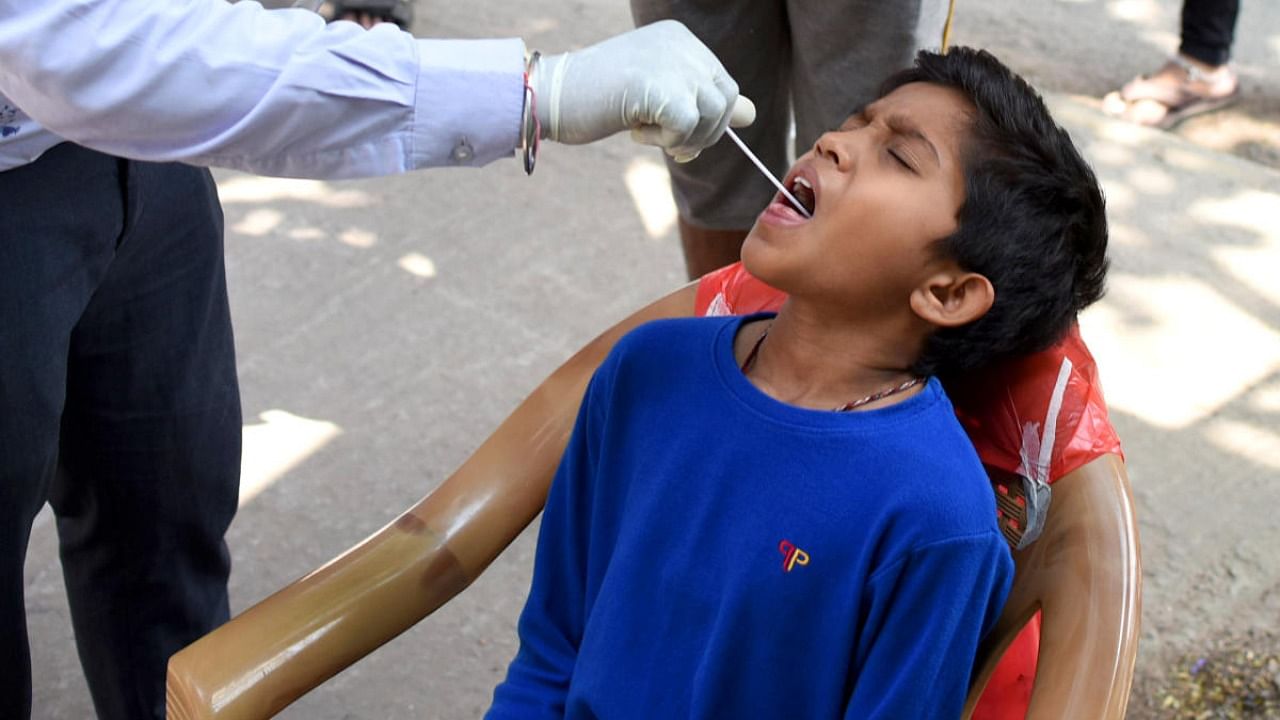 A healthcare worker takes a boy's swab samples for Covid-19 testing in RR Nagar on Tuesday. Credit: DH Photo