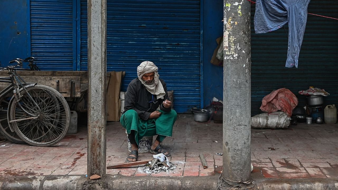 A migrant labourer sits close to a bonfire next to a closed shop at a market area in the walled city of Delhi during a weekend curfew imposed to curb the spread of Covid-19 coronavirus in New Delhi on January 15, 2022 as per the directive of the Delhi government. Credit: AFP File Photo