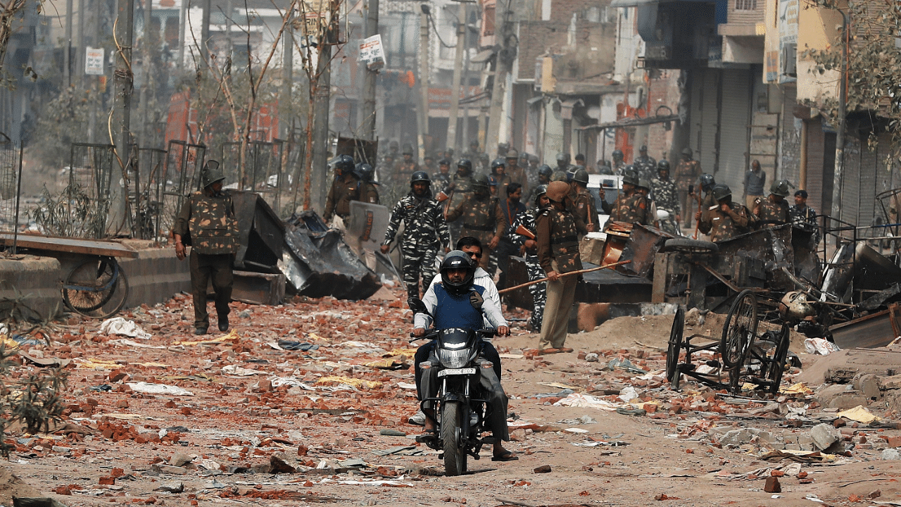 Men ride a motorcycle past security forces patrolling a street in a riot affected area after clashes erupted between people demonstrating for and against a new citizenship law in New Delhi. Credit: Reuters Photo