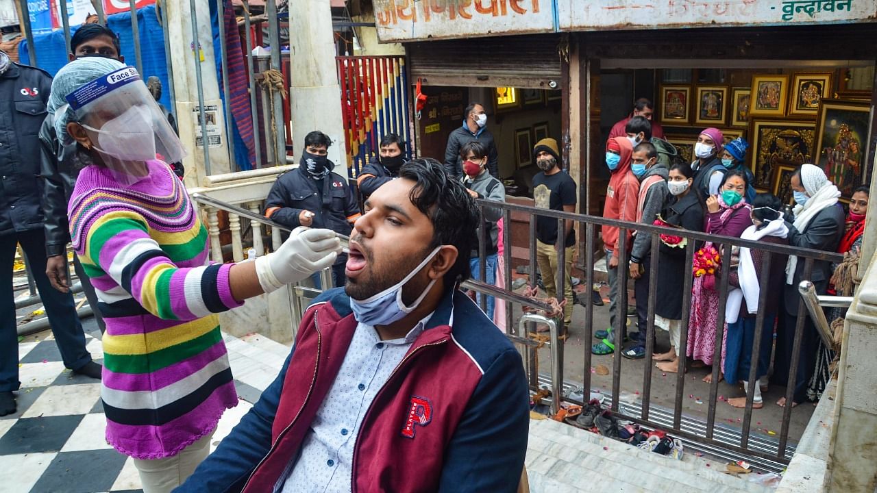 A health worker collects a swab sample of a devotee for Covid-19 test, outside Sri Bankey Bihari temple in Vrindavan. Credit: PTI File Photo