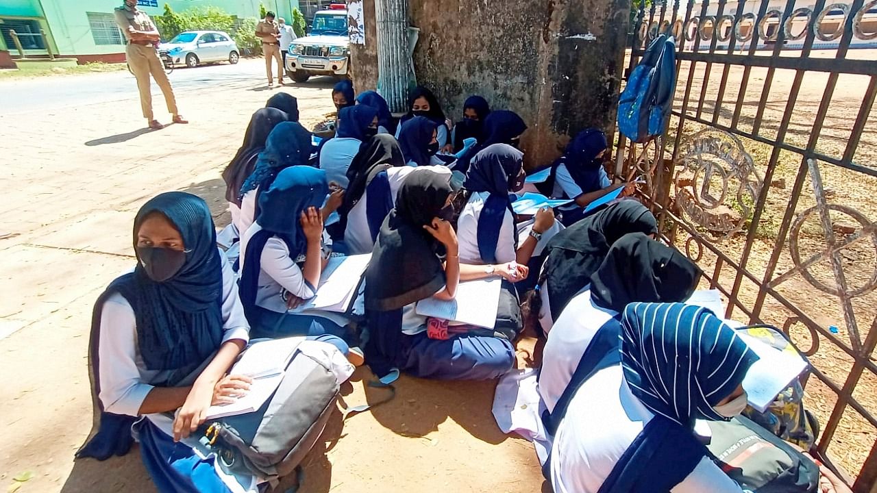 Students wearing hijab sit outside their school as the school authorities denied entry for wearing a hijab or scarf, in Kundapura of Udupi. Credit: PTI Photo