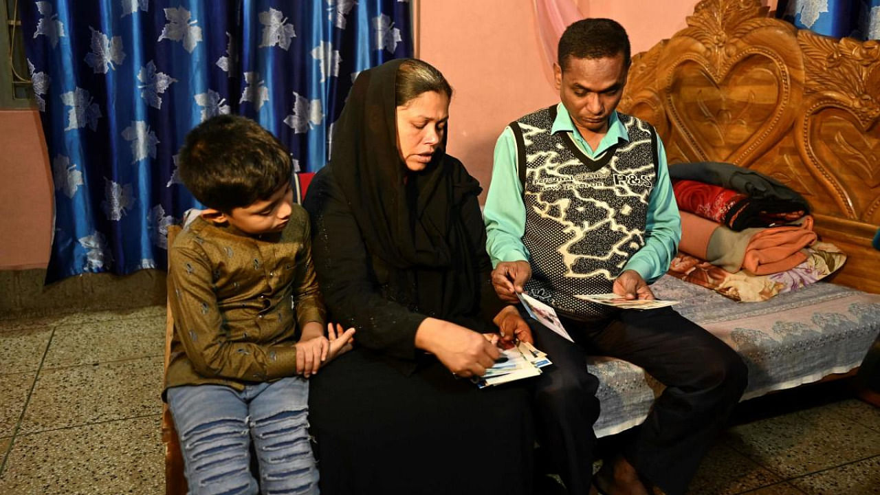 In this picture taken on February 9, 2022, father Mohsin Howlader (R), mother Rita Begum (C) and younger brother of Rakib Howlader, a 14-year-old boy who died during his arrest by the police in 2018, look at his pictures during an interview with AFP at their house in Dhaka. Credit: AFP Photo