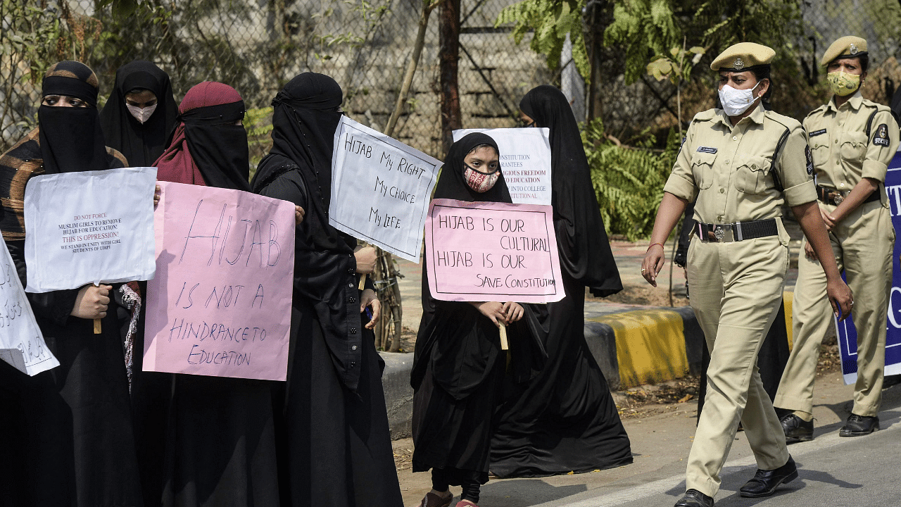 Police officers walk past members of the Muslim Women Association as they hold placards along a roadside during a silent protest after few Karnataka's educational institutes denied entry to students wearing hijabs. Credit: PTI Photo