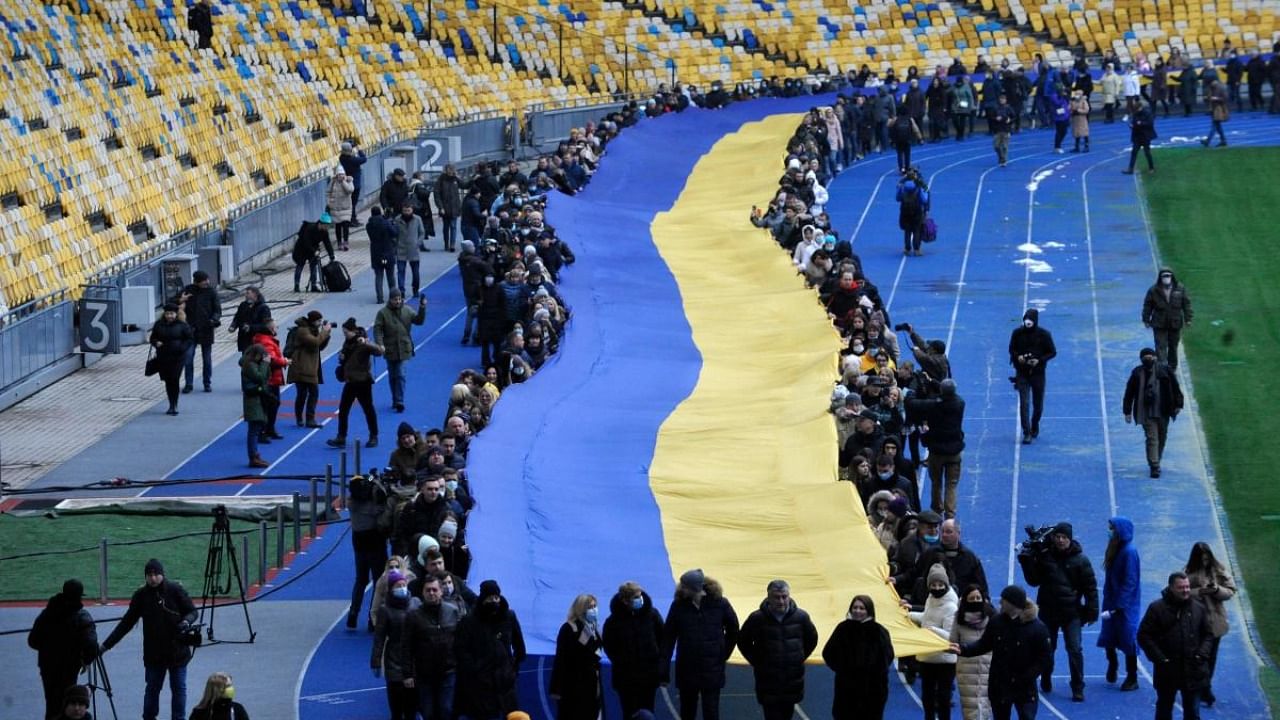 People carry a giant Ukraine's national flag at a stadium to mark a "Day of Unity" in Kyiv on February 16, 2022. Credit: AFP Photo