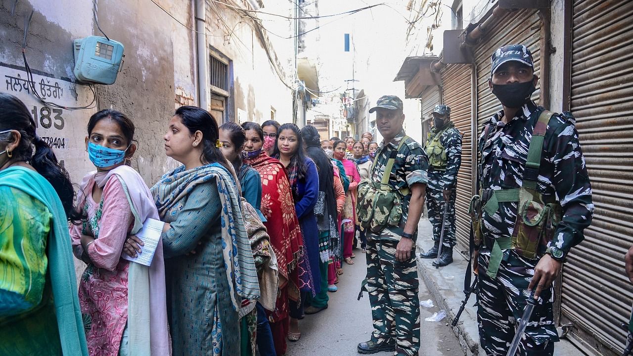 Security personnel stand guard as voters wait to cast their vote during the Punjab Assembly elections, in Jalandhar. Credit: PTI Photo