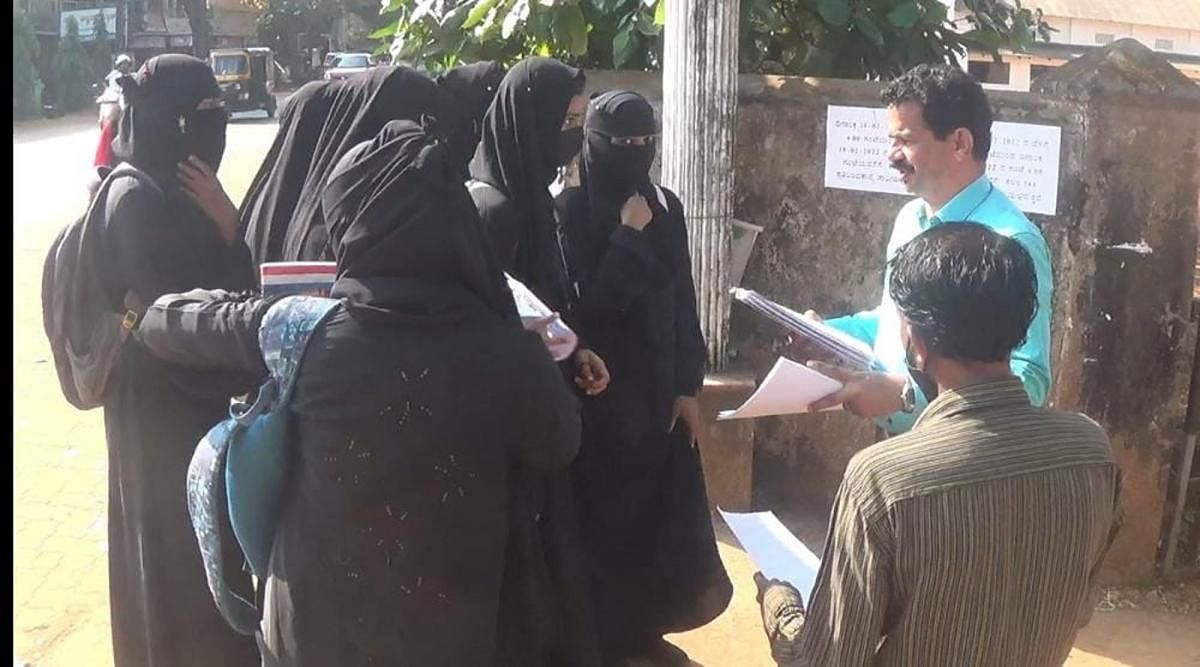 Girl students wearing hijab submit their assignments to a lecturer at the gate of the government junior college in Kundapura.