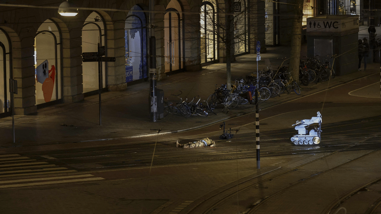 A man in camouflage clothing lies next to a police robot in a street after the hostage-taking ended in Amsterdam. Credit: AFP Photo