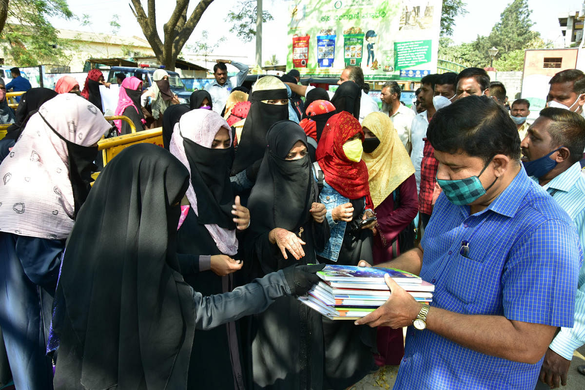 Hijab-clad girls submit their assignment to college staff at the entrance of government pre-university college for girls in Chitradurga on Tuesday. Credit: DH Photo