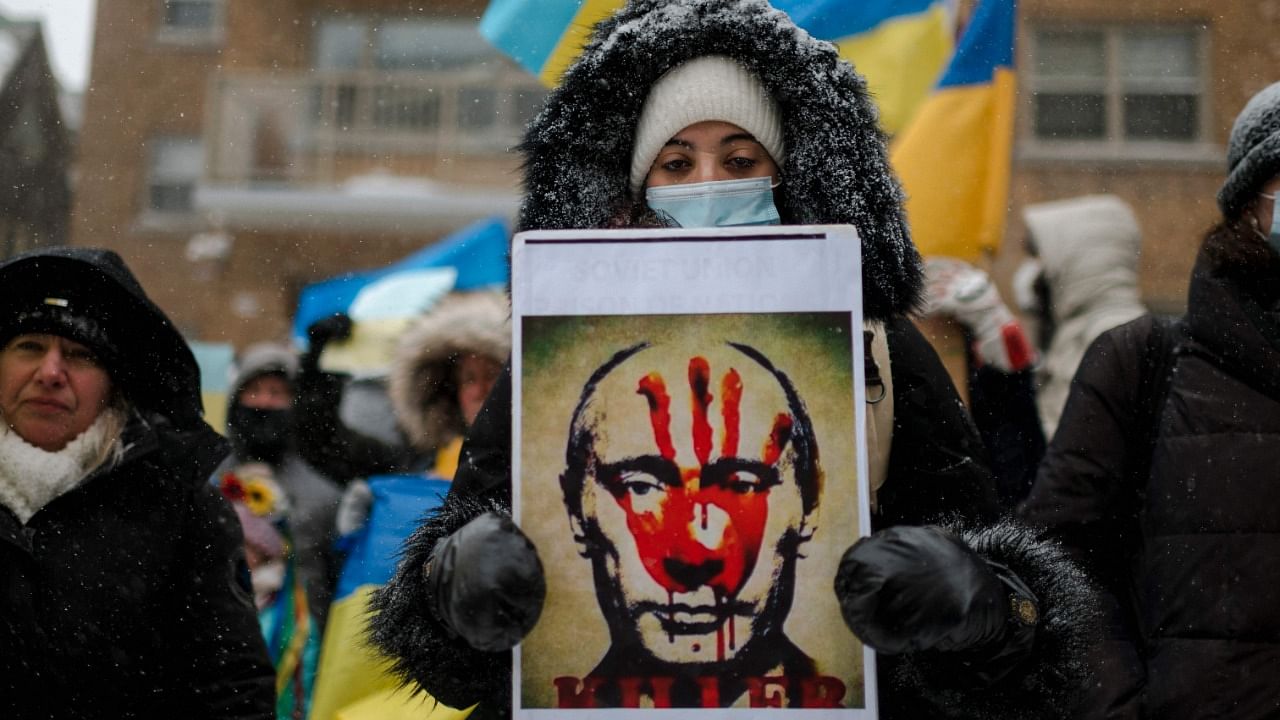 A woman holds a portrait of Russian president Vladimir Putin with a bloody hand on his face as members of the Ukrainian community protest in front of the Consulate General of the Russian Federation on February 25, 2022 in Montreal, Quebec. Credit: AFP Photo