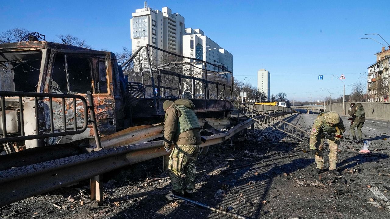 Ukrainian soldiers investigate debris of a burning military truck on a street in Kyiv, Ukraine, Saturday, Feb. 26, 2022. Russian troops stormed toward Ukraine's capital Saturday, and street fighting broke out as city officials urged residents to take shelter. Credit: AP/PTI Photo