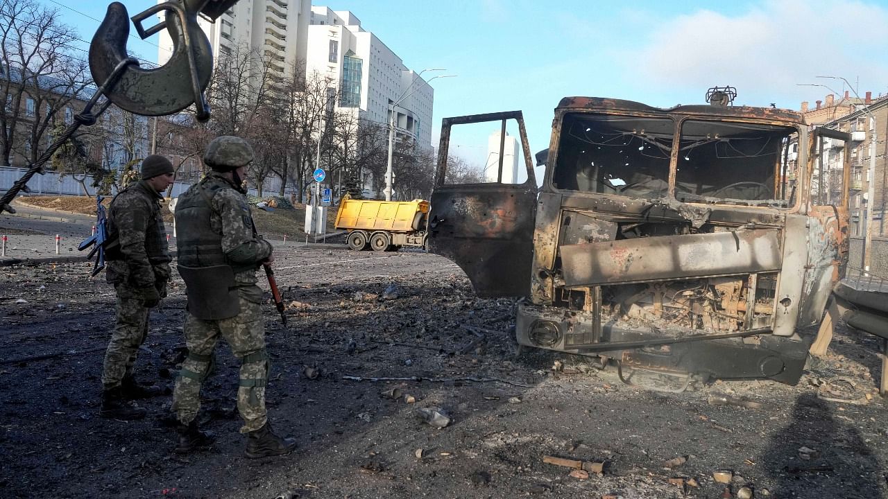 Ukrainian soldiers stand next to a burnt military truck, in a street in Kyiv, Ukraine, Saturday, Feb. 26, 2022. Russian troops stormed toward Ukraine's capital Saturday, and street fighting broke out as city officials urged residents to take shelter. Credit: AP/PTI Photo