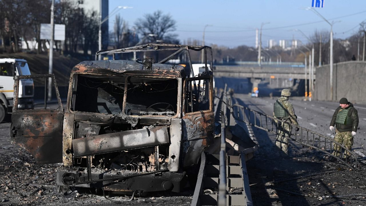 Ukrainian soldiers stand past a burnt Ukrainian army vehicle on the west side of the Ukrainian capital of Kyiv. Credit: AFP File Photo