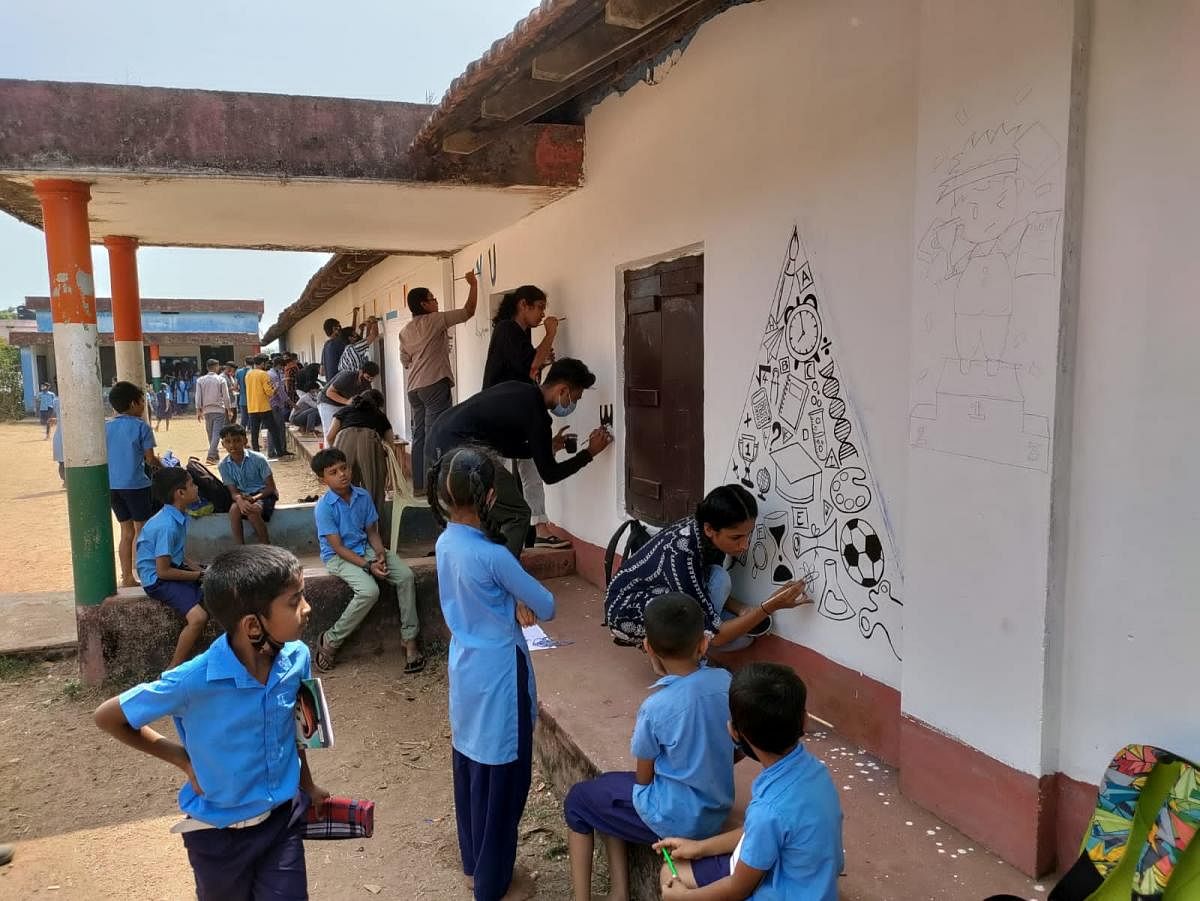 Students of DK ZP Government Higher Primary School, Valachil, watch as students of Srinivas School of Architecture create artworks on the wall of the school. DH Photo