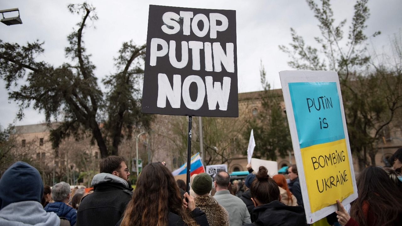 Demonstrators hold signs reading "Putin is bombing Ukraine" and "Stop Putin Now" during a protest against Russia's military operation in Ukraine, in Barcelona. Credit: AFP Photo