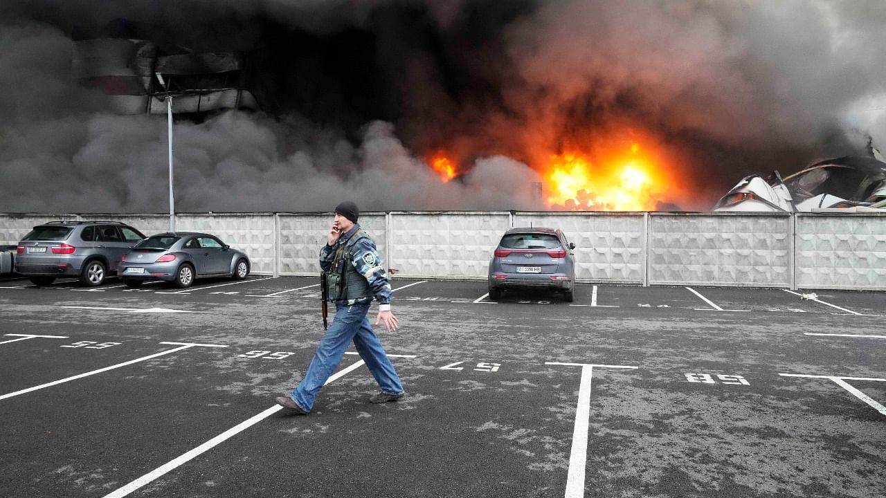 A Ukrainian serviceman walks past as fire and smoke rises over a damaged logistic center after shelling in Kyiv, Ukraine, Thursday, March 3, 2022. Russian forces have escalated their attacks on crowded cities in what Ukraine's leader called a blatant campaign of terror. Credit: AP/PTI Photo