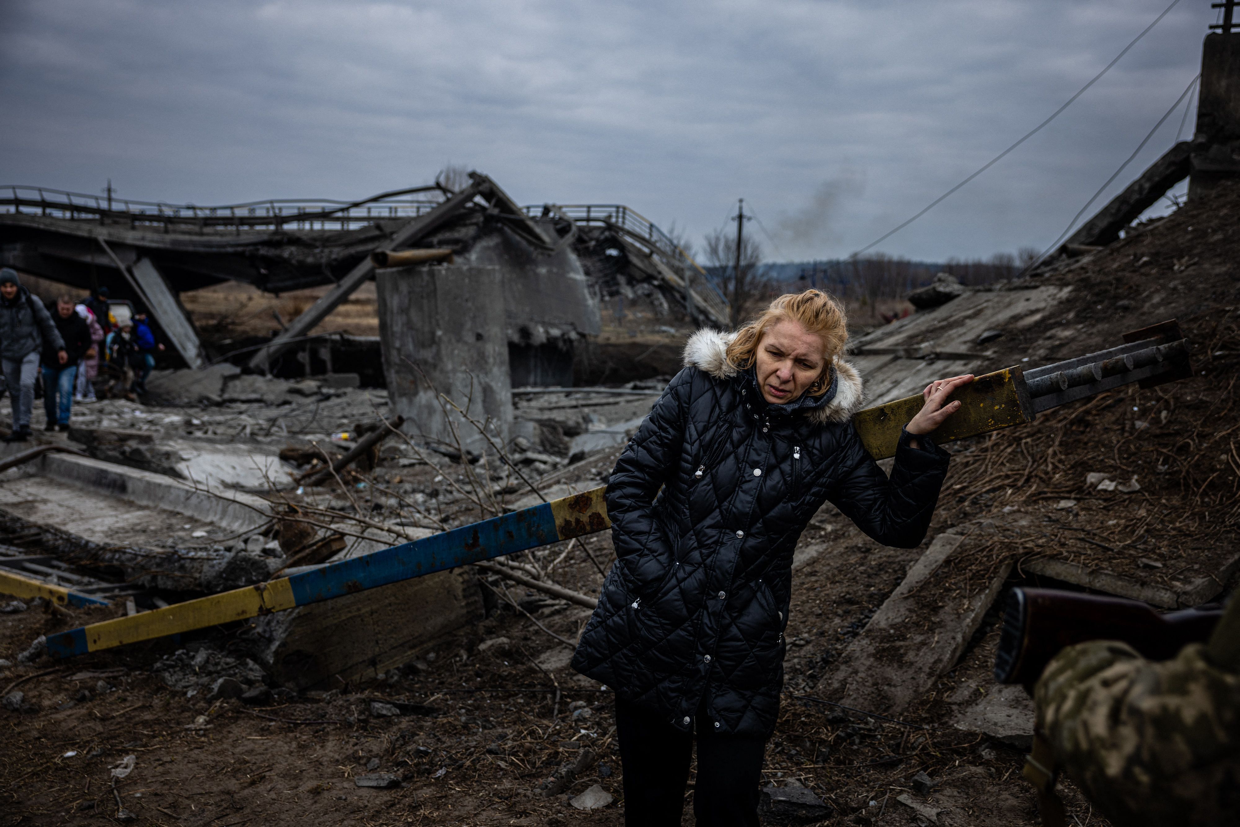 A woman takes a rest after crossing a destroyed bridge as she evacuates from the city of Irpin. Credit: AFP File Photo