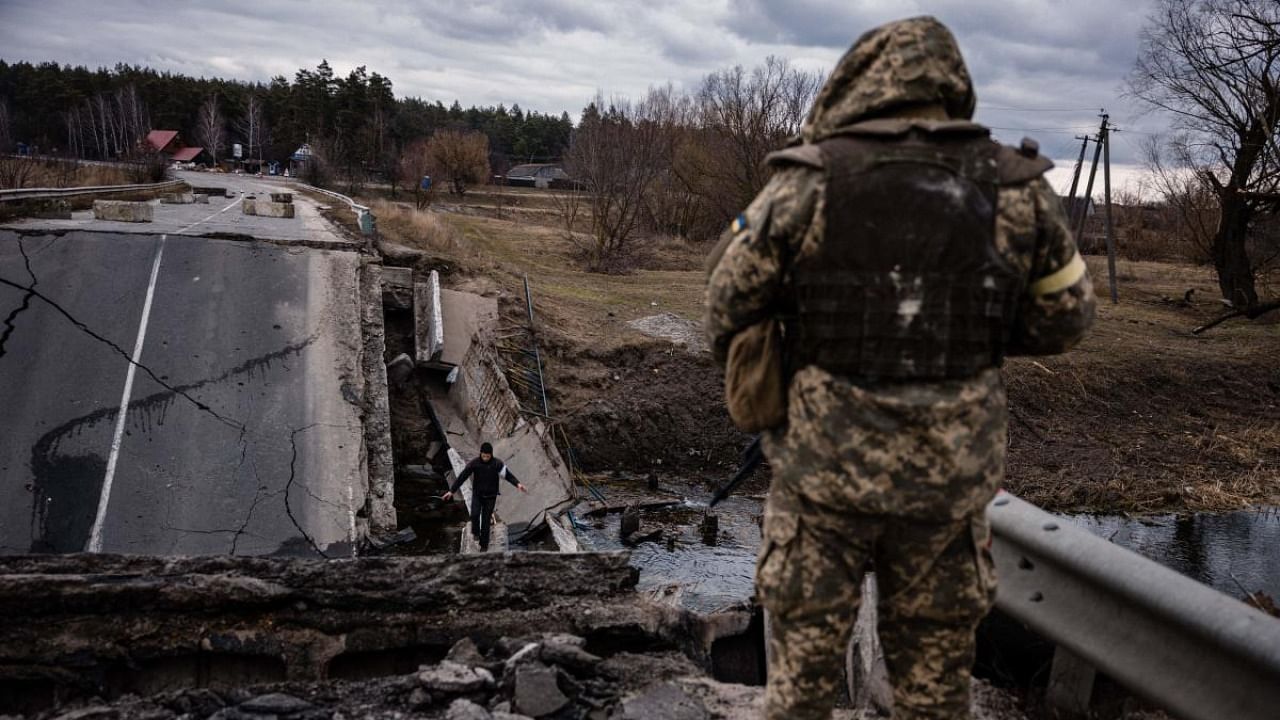 An Ukrainian serviceman looks at a civilian crossing a blown up bridge in a village, east of the town of Brovary on March 6, 2022. Credit: AFP Photo