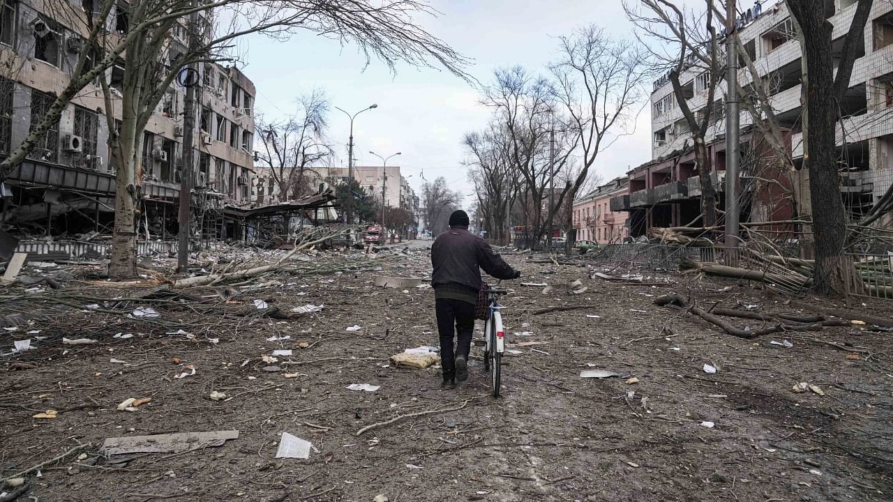  A man walks with a bicycle in a street damaged by shelling in Mariupol. Credit: AP Photo