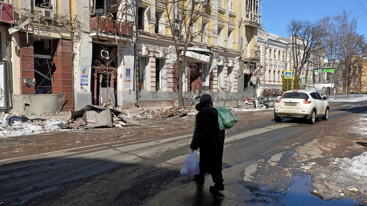 A woman crosses a street in front of a damaged buildings in Kharkiv. Credit: AFP Photo