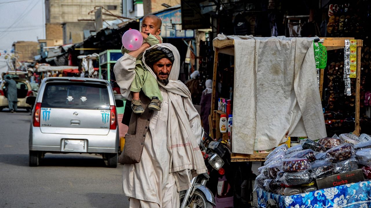 An Afghan man carries a child on his shoulders as he walks along a road next to a market area in Kandahar. Credit: AFP File Photo