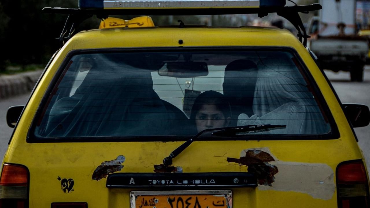 An Afghan girl travelling with other burqa clad women peeps out of a car window in Kandahar on March 12, 2022. Credit: AFP Photo