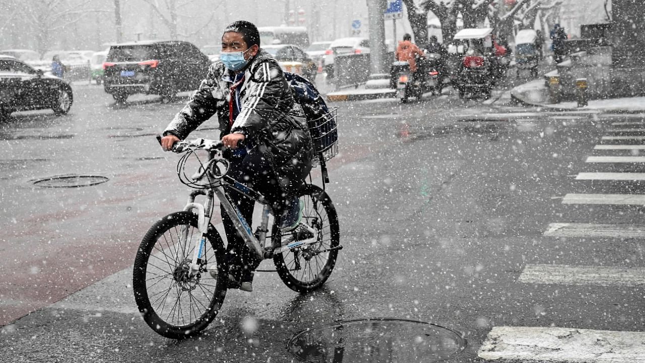 A boy rides a bike along a street on a snowy day in Beijing on March 18, 2022. Credit: AFP Photo