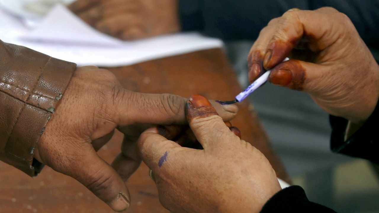 A polling official inks the finger of a voter at a polling booth let him cast his vote during the first phase of the District Development Council (DDC) elections, in Hariganiwan area of Gund in Ganderbal district of central Kashmir. Credit: PTI File Photo
