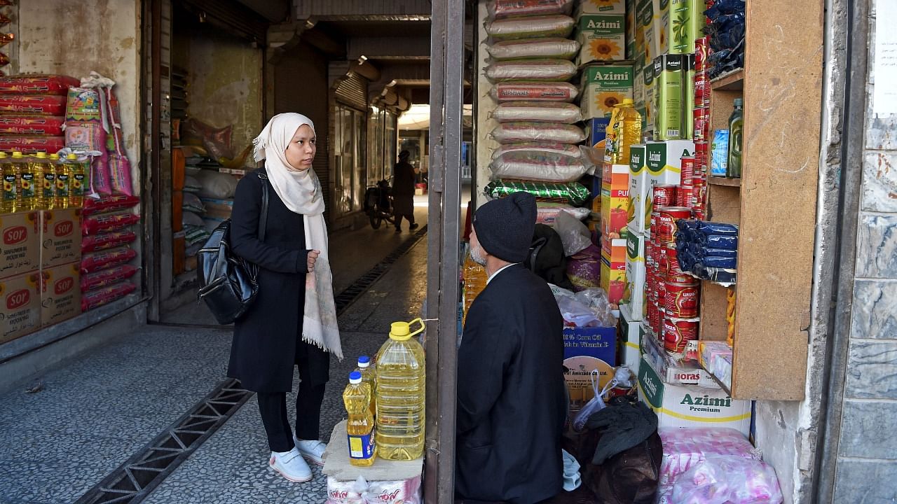 In this photo taken on February 15, 2022, university student Arezo Akrimi (L) buys groceries after exchanging her cryptocurrency for cash at a market in Herat. Credit: AFP Photo