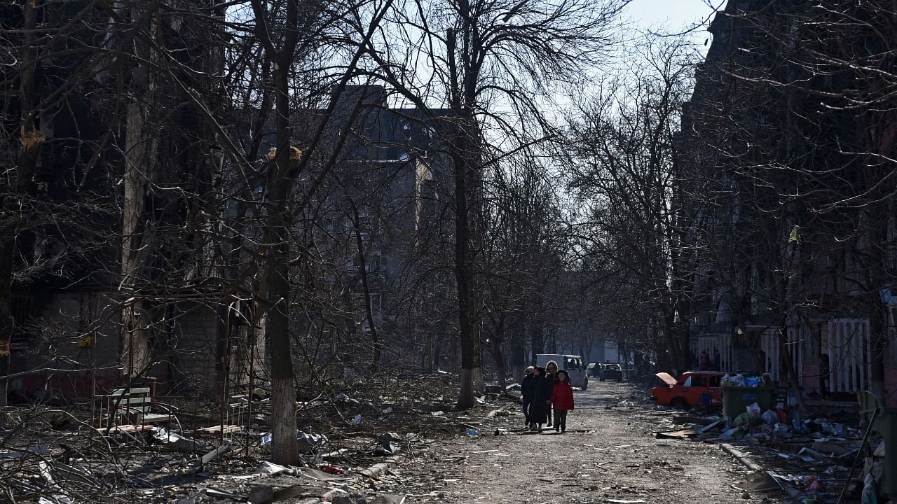 Local residents walk near damaged residential buildings in the besieged city of Mariupol. Credit: Reuters Photo