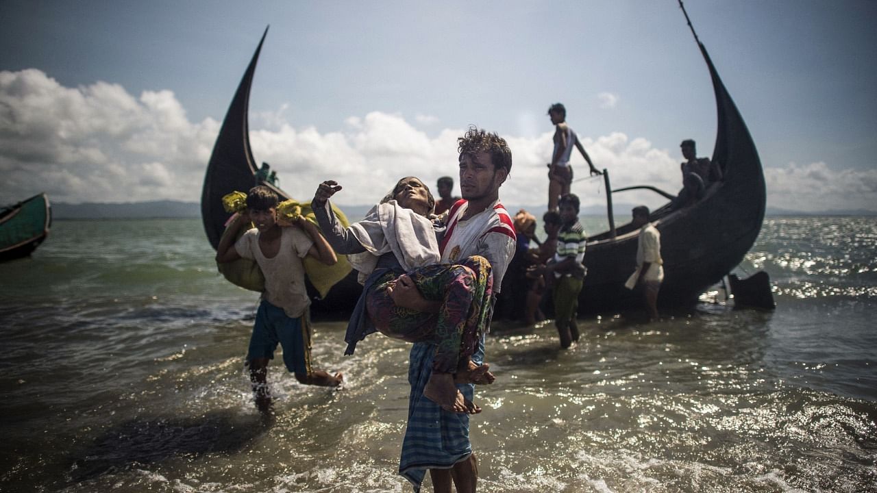 A Bangladeshi man helps Rohingya Muslim refugees to disembark from a boat on the Bangladeshi shoreline of the Naf river after crossing the border from Myanmar in Teknaf. Credit: AFP File Photo