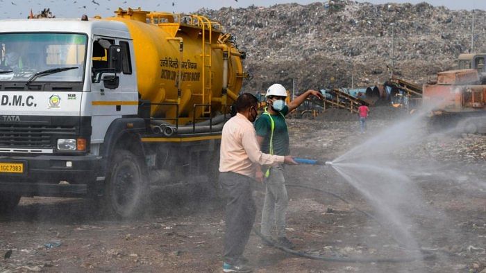 An employee of Municipal Corporation of Delhi (MCD) north-zone sprays water to control the dust at Bhalswa landfill in New Delhi. Credit: AFP