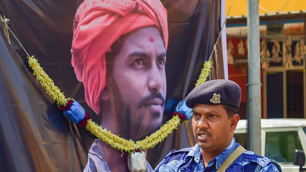 A RAF officer stands at guard in front of a poster of Bajrang dal activist Harsha. Credit: PTI Photo