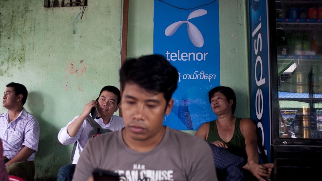 In this file photo taken on September 26, 2014, a man uses a mobile phone in front of a Telenor advertising board in Yangon. Credit: AFP photo